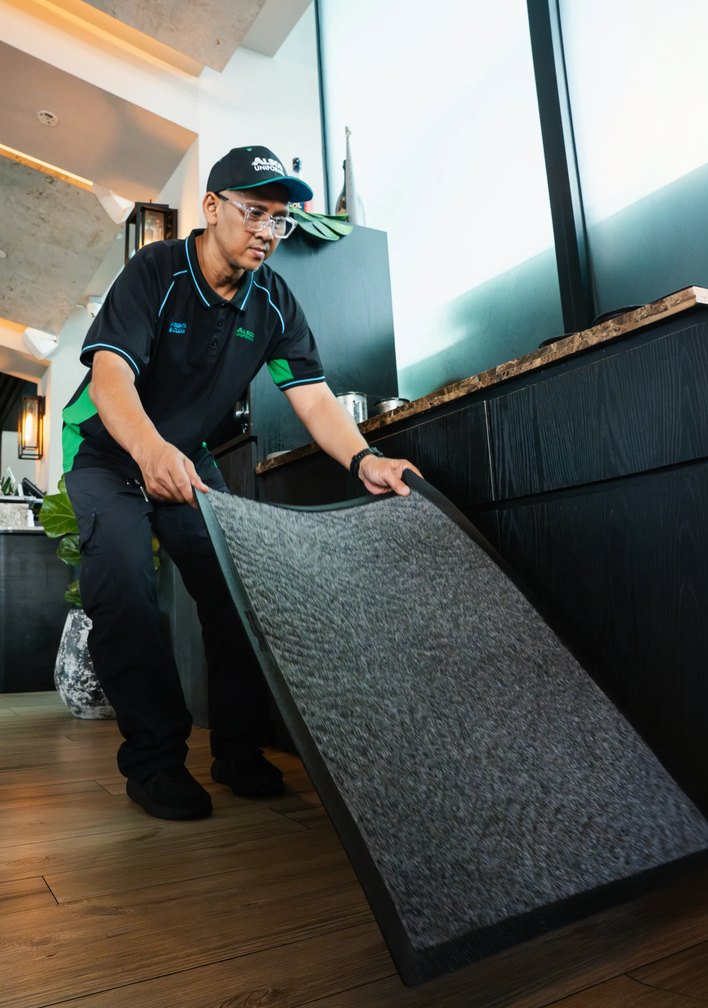 Alsco service technician laying a grey commercial floor mat inside a modern restaurant