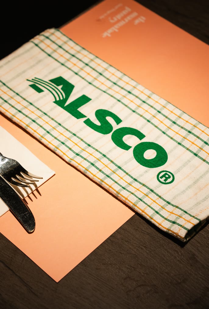 Checked tea towel with the green Alsco logo on a dining table beside cutlery