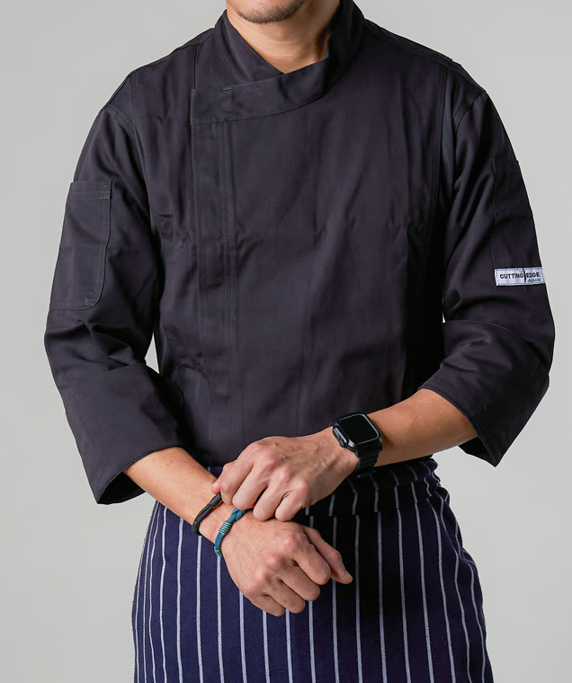 Chef wearing a black Cutting Edge chef coat over a navy striped apron