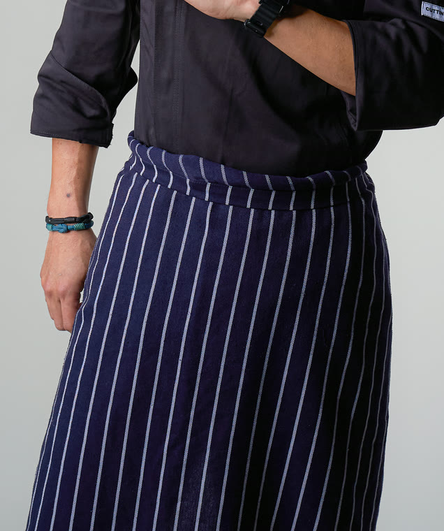 Navy and white pinstripe chef apron worn over a black chef coat