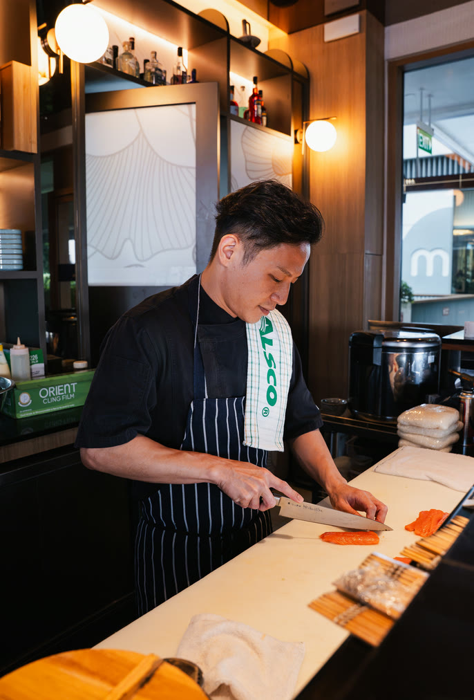 Chef in a black shirt and striped apron with an Alsco tea towel preparing food at a restaurant counter