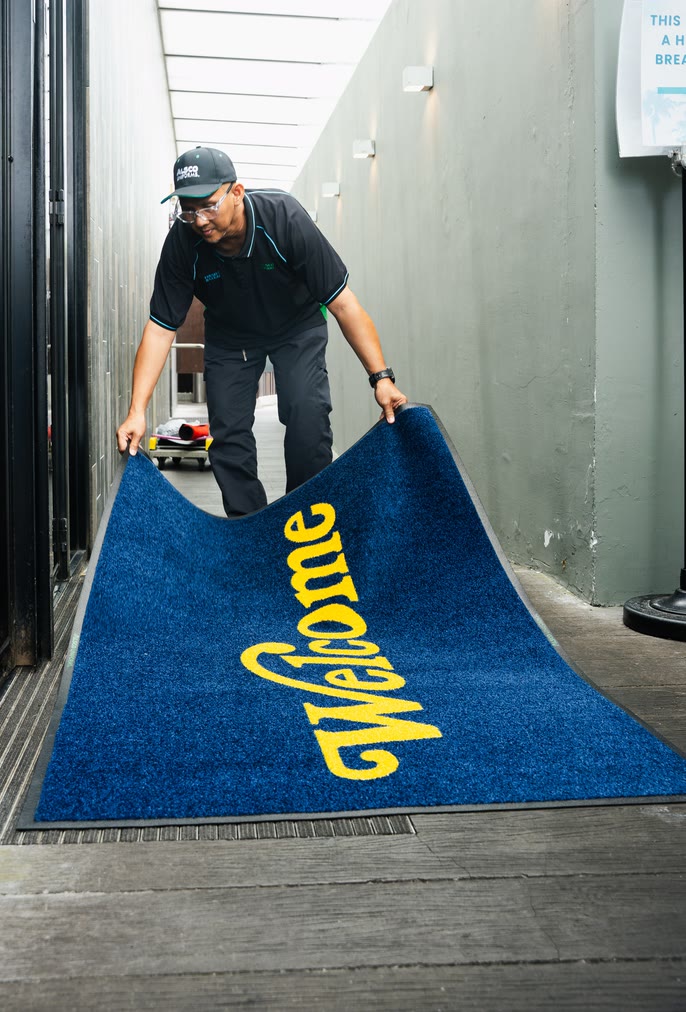 Worker laying a blue Welcome entrance mat in a building corridor