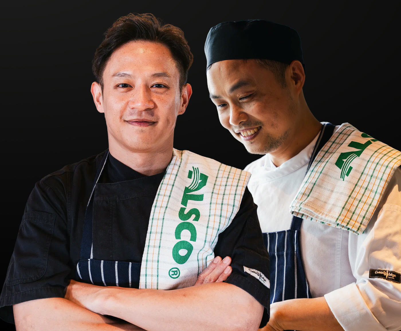 Two smiling chefs in Cutting Edge chef jackets and striped aprons with Alsco tea towels on their shoulders